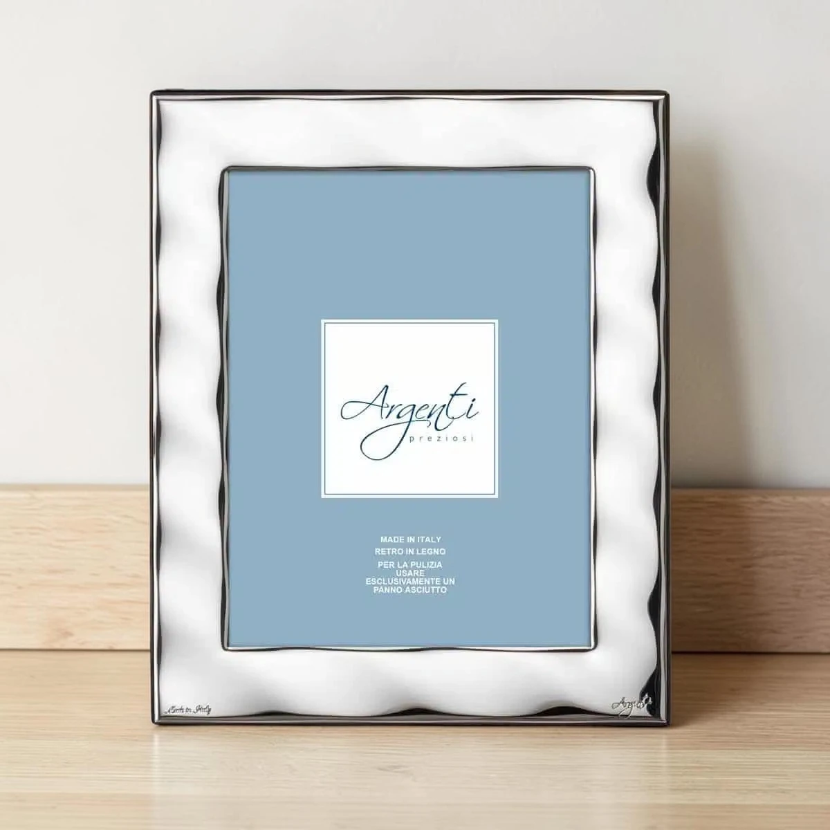 Cornice portafoto in argento con bordo ad onde appoggiata su un mobile in legno