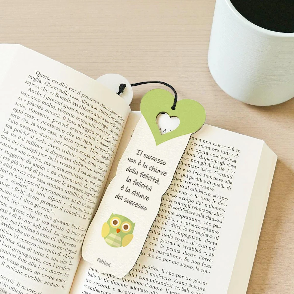 Foto ambientata del segnalibro bomboniera con gufetto verde portafortuna, appoggiato su un libro aperto