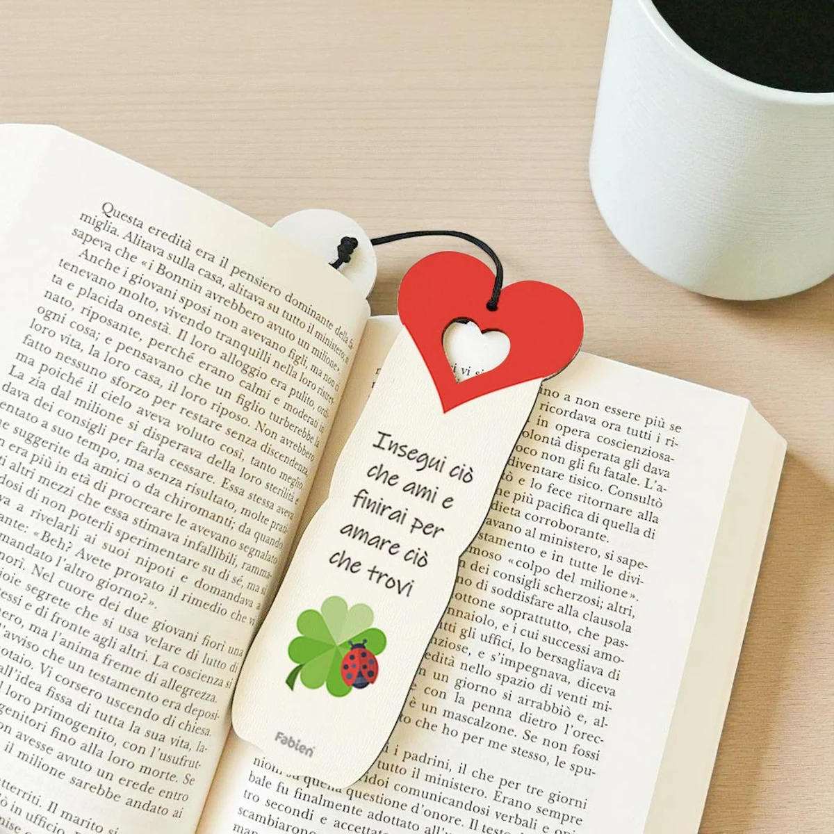 Foto ambientata del segnalibro bomboniera con quadrifoglio verde e coccinella portafortuna, appoggiato su un libro aperto