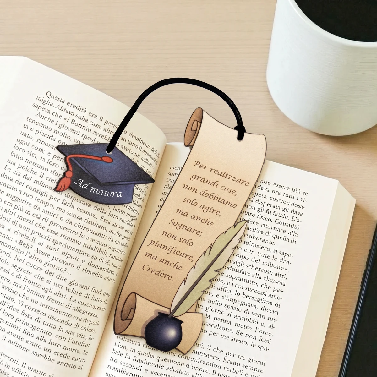 Segnalibro laurea Ad Maiora in legno appoggiato tra le pagine di un libro aperto, con ciondolo a tocco di laurea